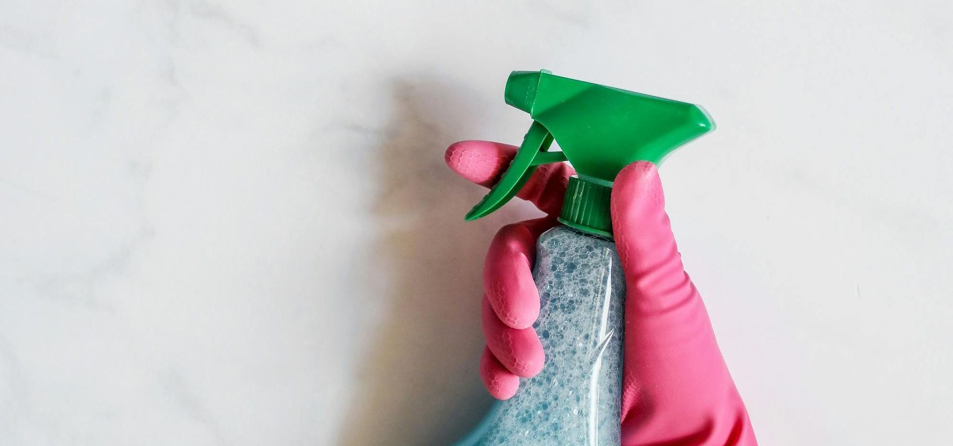 A person wearing pink gloves is holding a spray bottle.