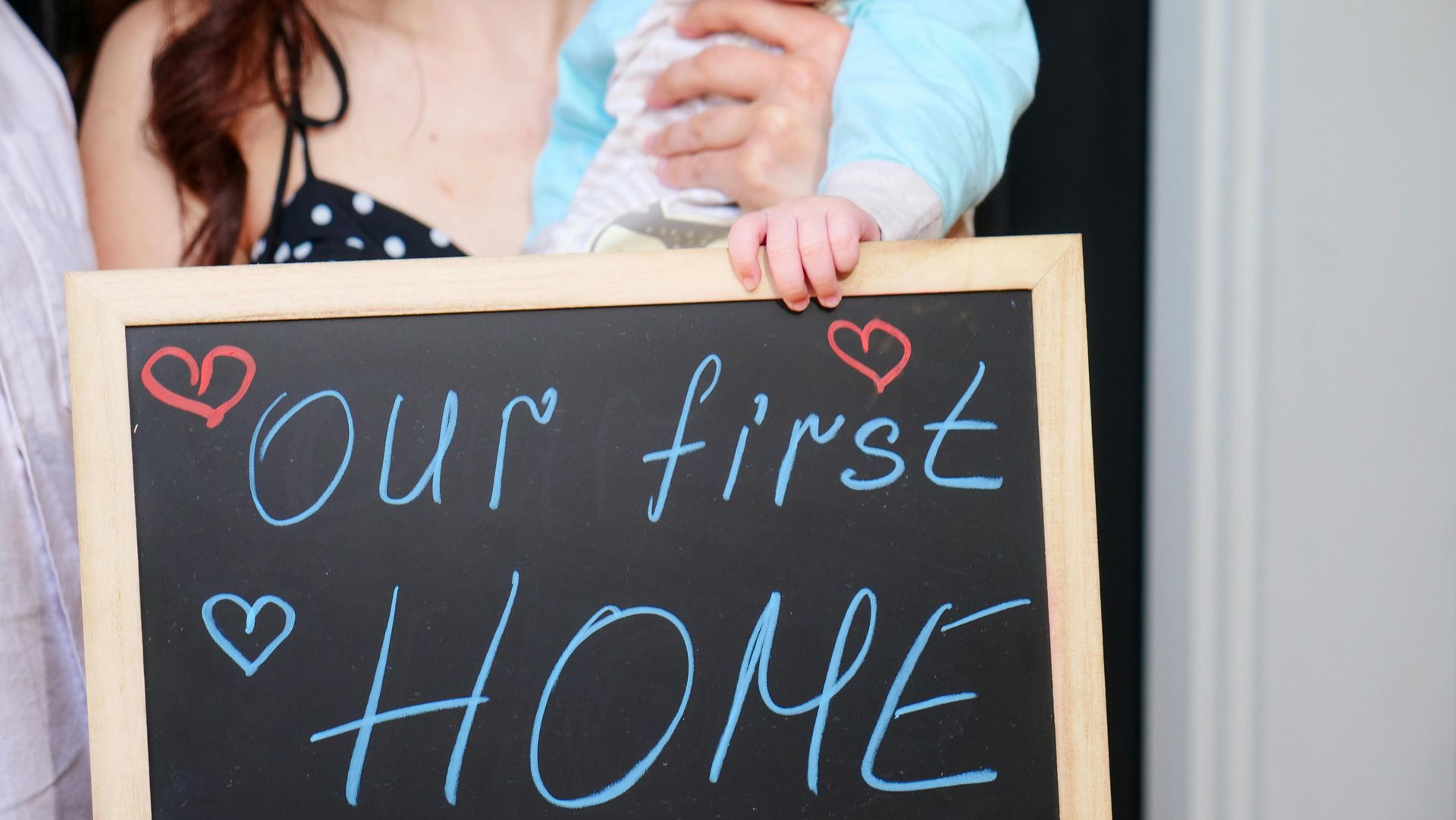 A woman is holding a baby and holding a chalkboard that says `` our first home ''.