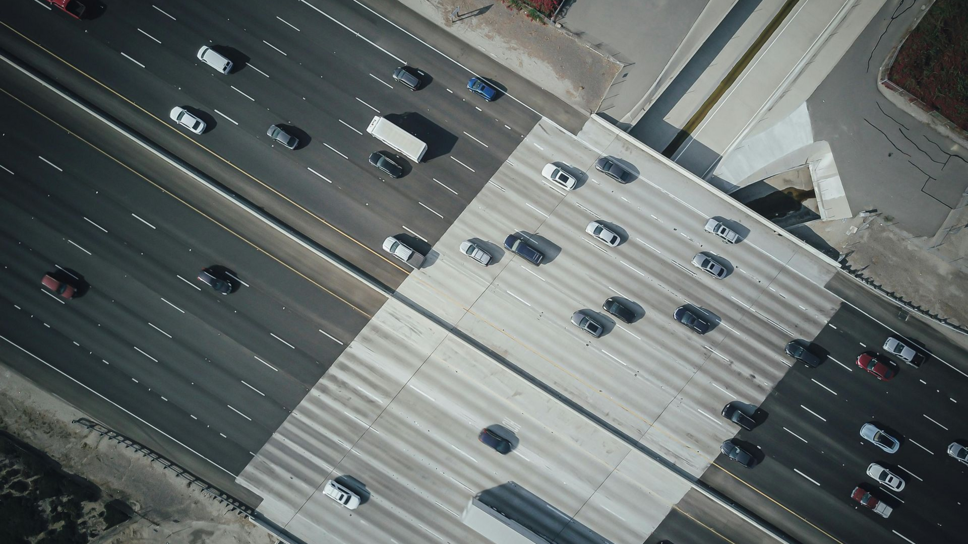 An aerial view of a multi-lane highway, with vehicles traveling across both asphalt and concrete bridge sections.