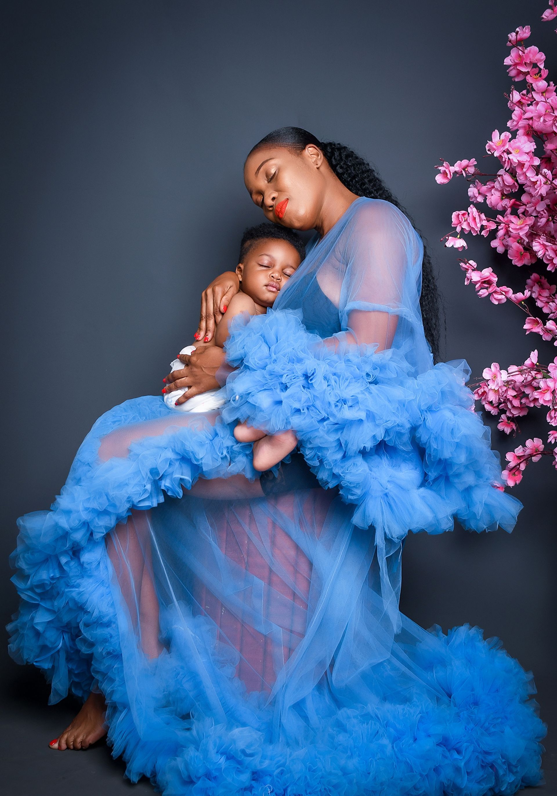 A woman in a blue dress is holding a baby in her arms.