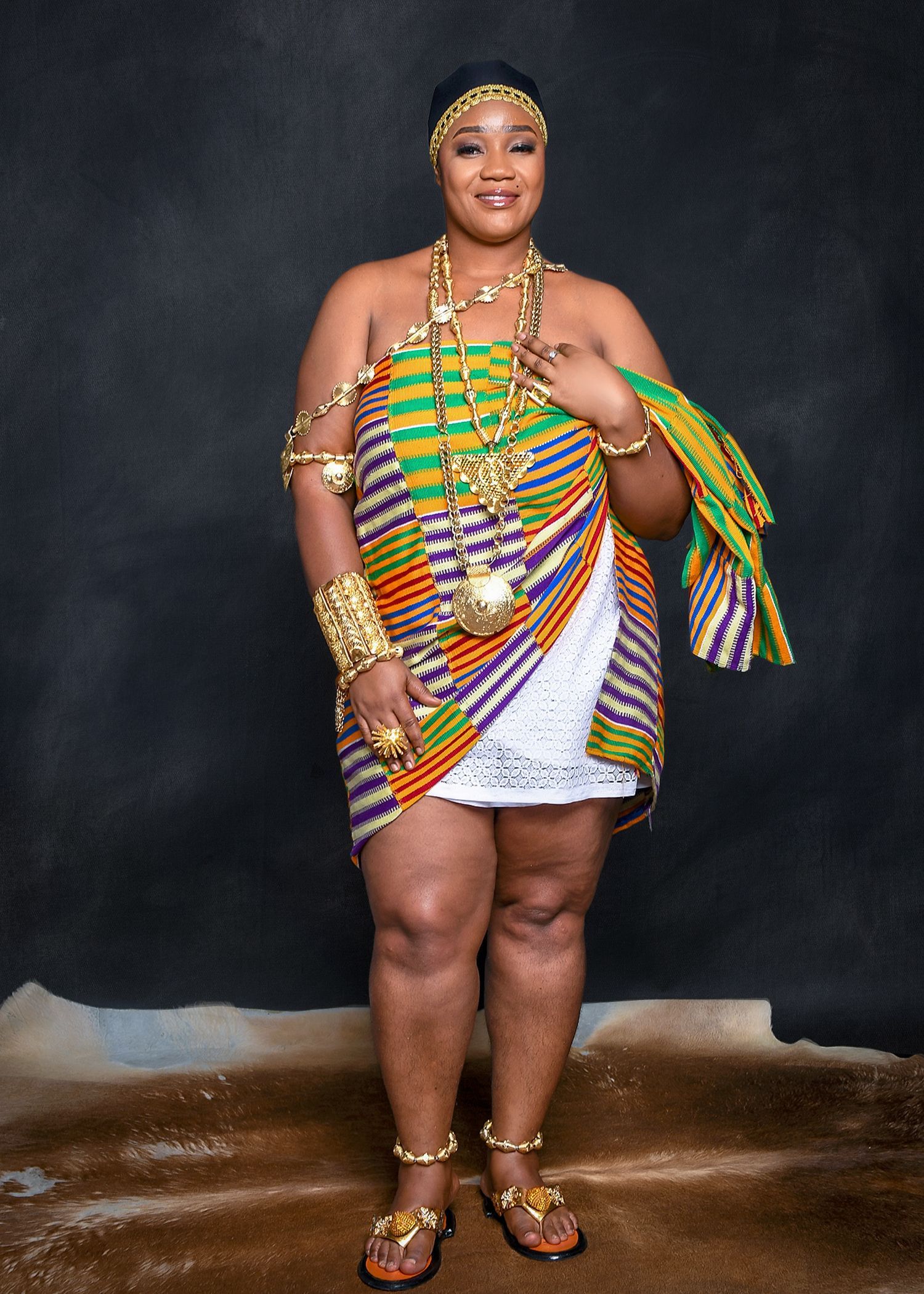 A woman in a colorful dress is standing in front of a black wall.