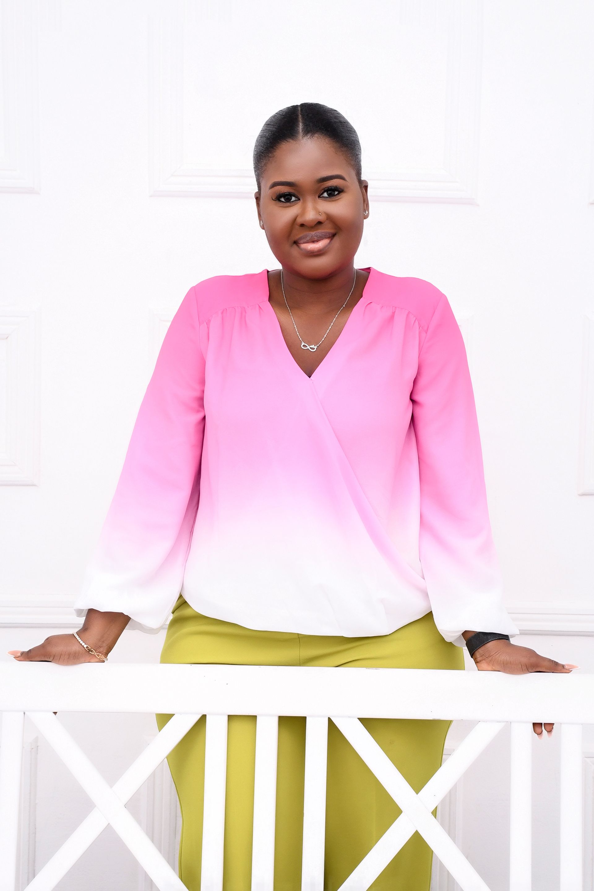 A woman in a pink and white blouse is leaning on a white railing.