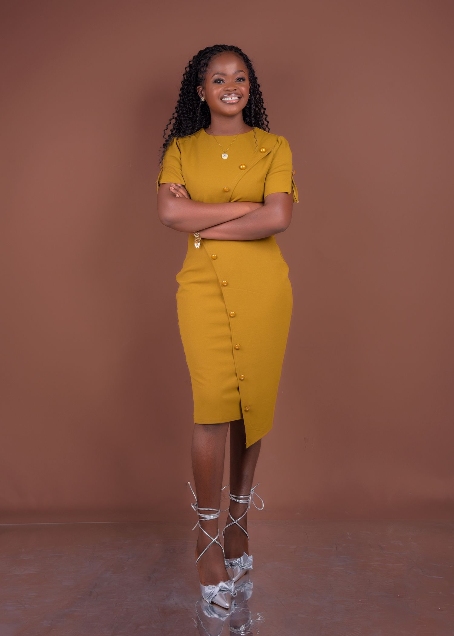 A woman in a yellow dress is standing with her arms crossed.