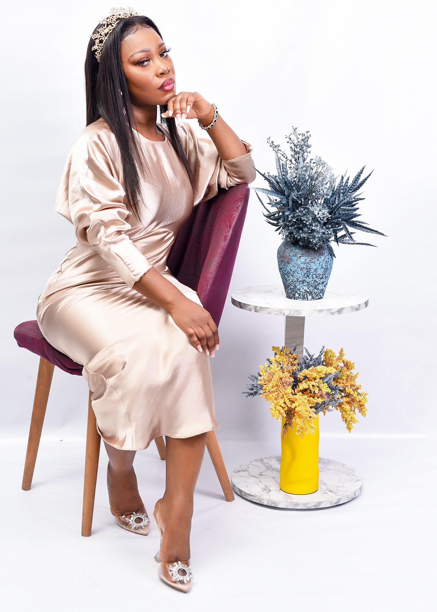 A woman in a dress is sitting on a chair next to a table with flowers.