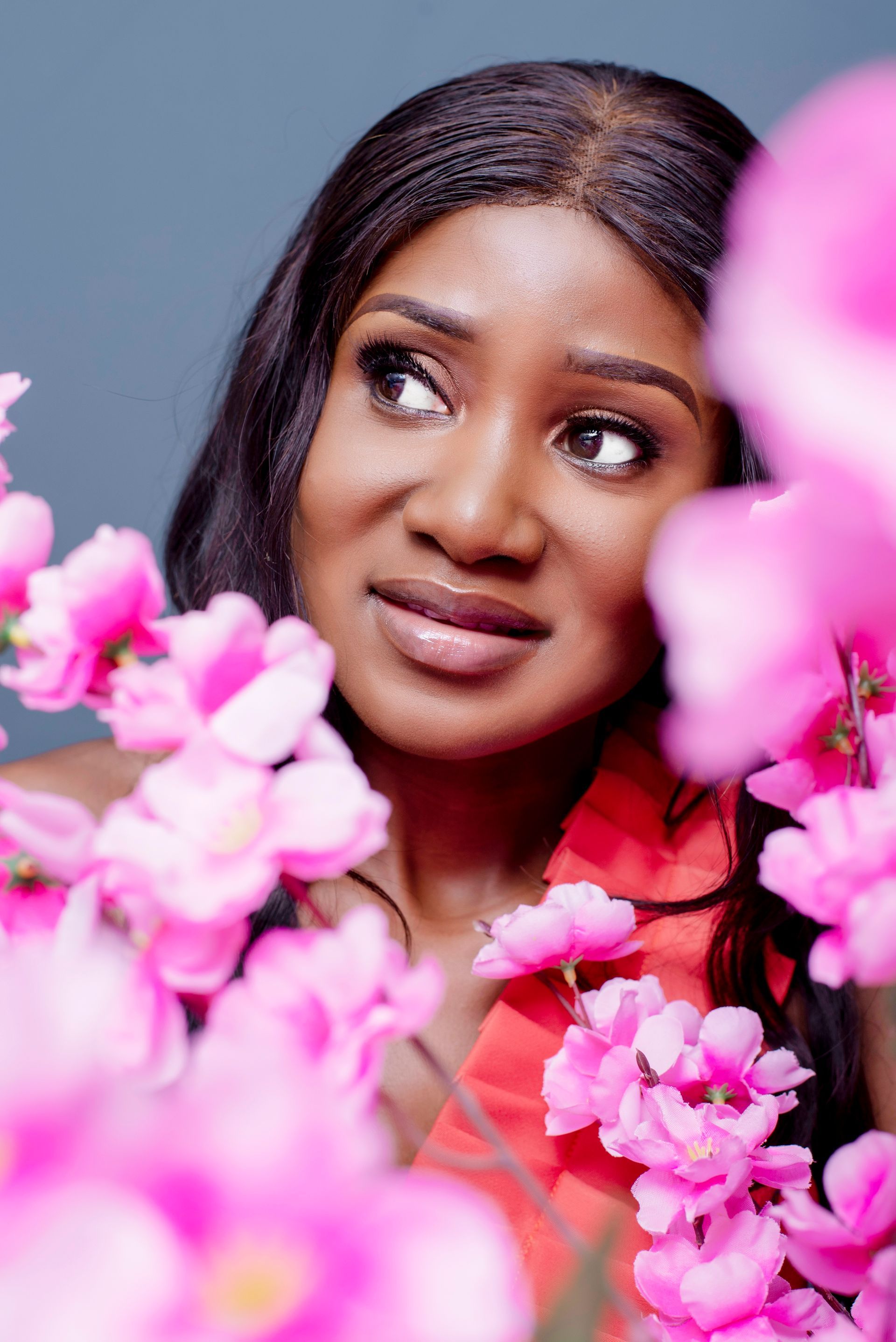 A woman in a red dress is surrounded by pink flowers.