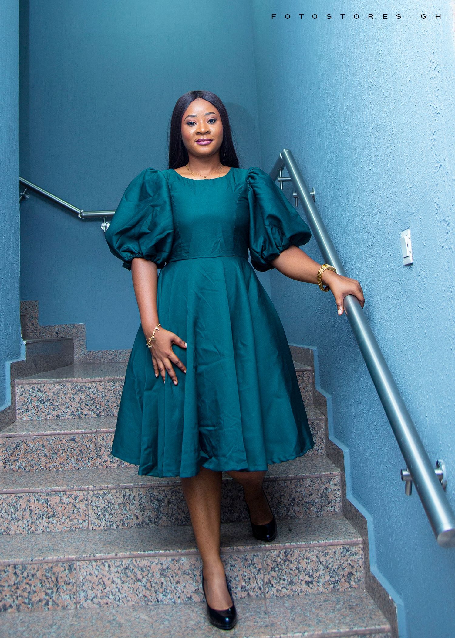 A woman in a green dress is standing on a set of stairs.