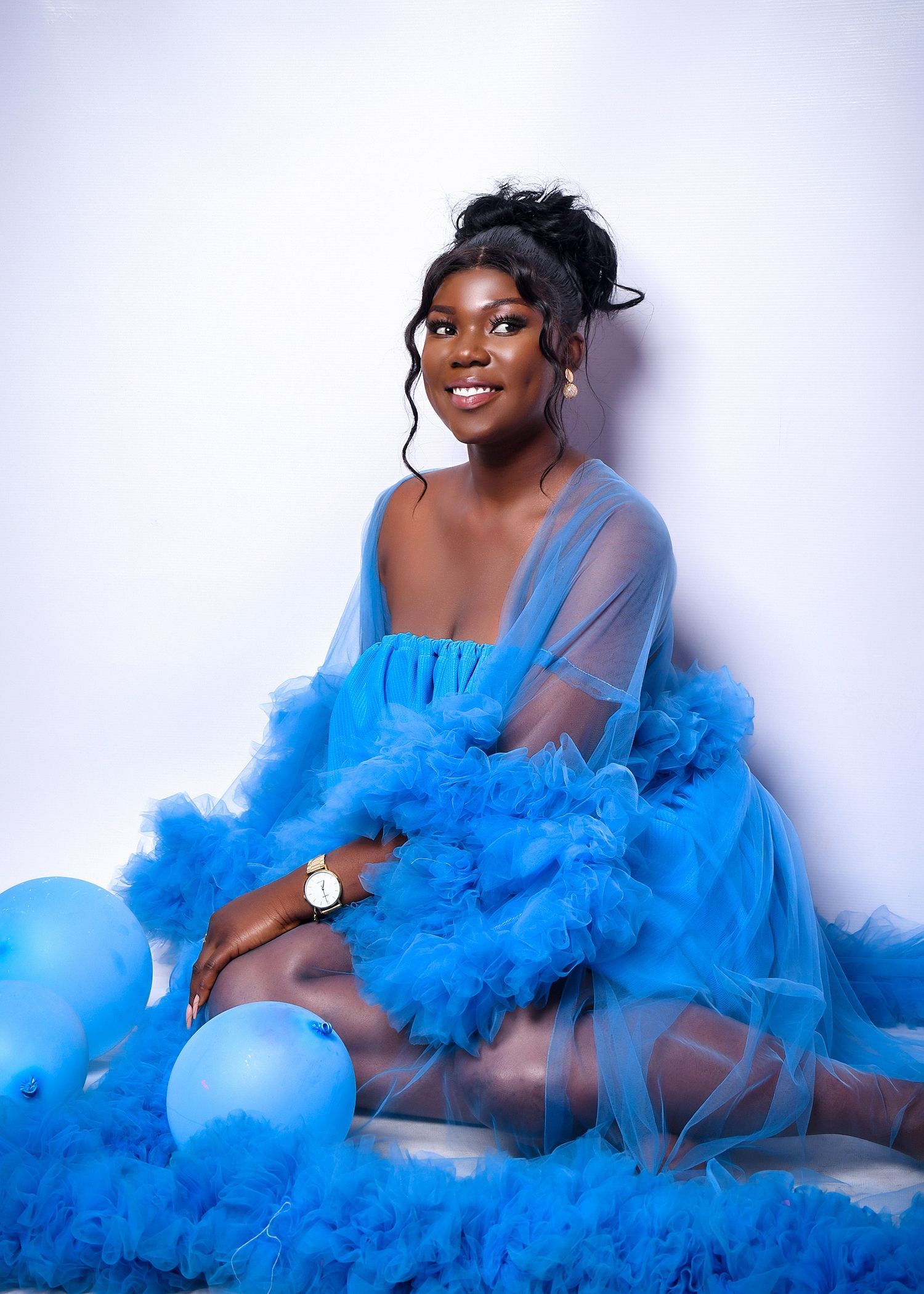 A woman in a blue dress is sitting on the floor surrounded by blue balloons.