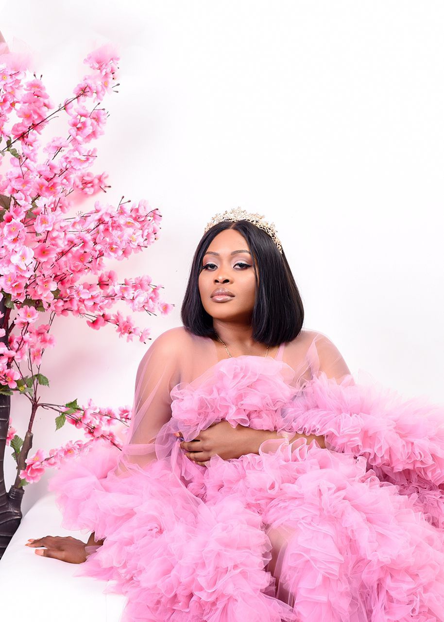 A pregnant woman is wearing a pink tulle dress and a crown.