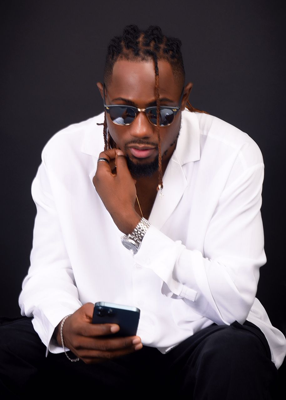 A man wearing sunglasses and a white shirt is holding a cell phone.
