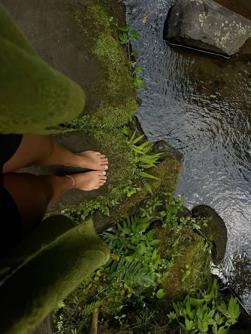 Woman standing barefoot on moss near a body of water