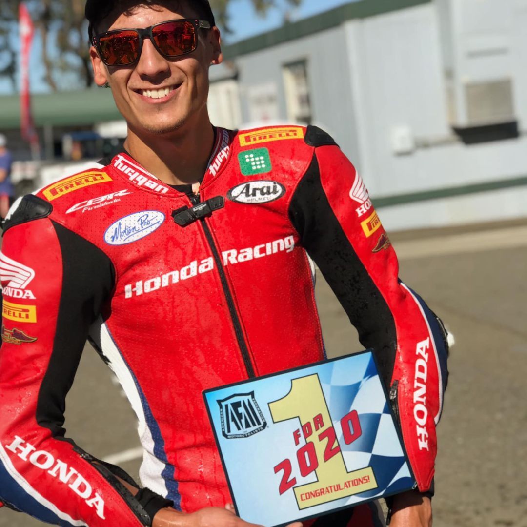 Smiling motorcycle racer in red Honda Racing suit holding a trophy plaque outdoors