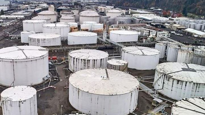 White storage tanks at an industrial facility, likely holding liquids, with a cloudy sky overhead.
