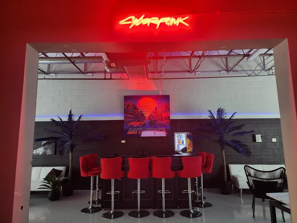 Cyberpunk-themed bar interior with red stools, neon sign, and wall art
