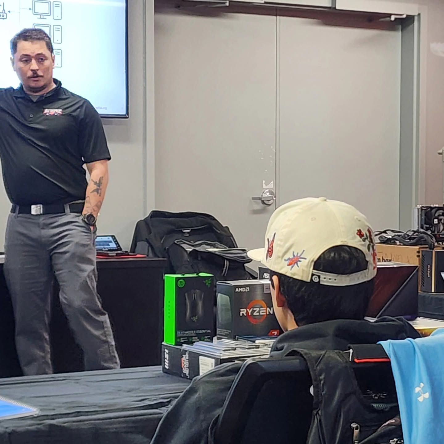 Instructor speaking in a classroom, with seated attendees in the foreground.
