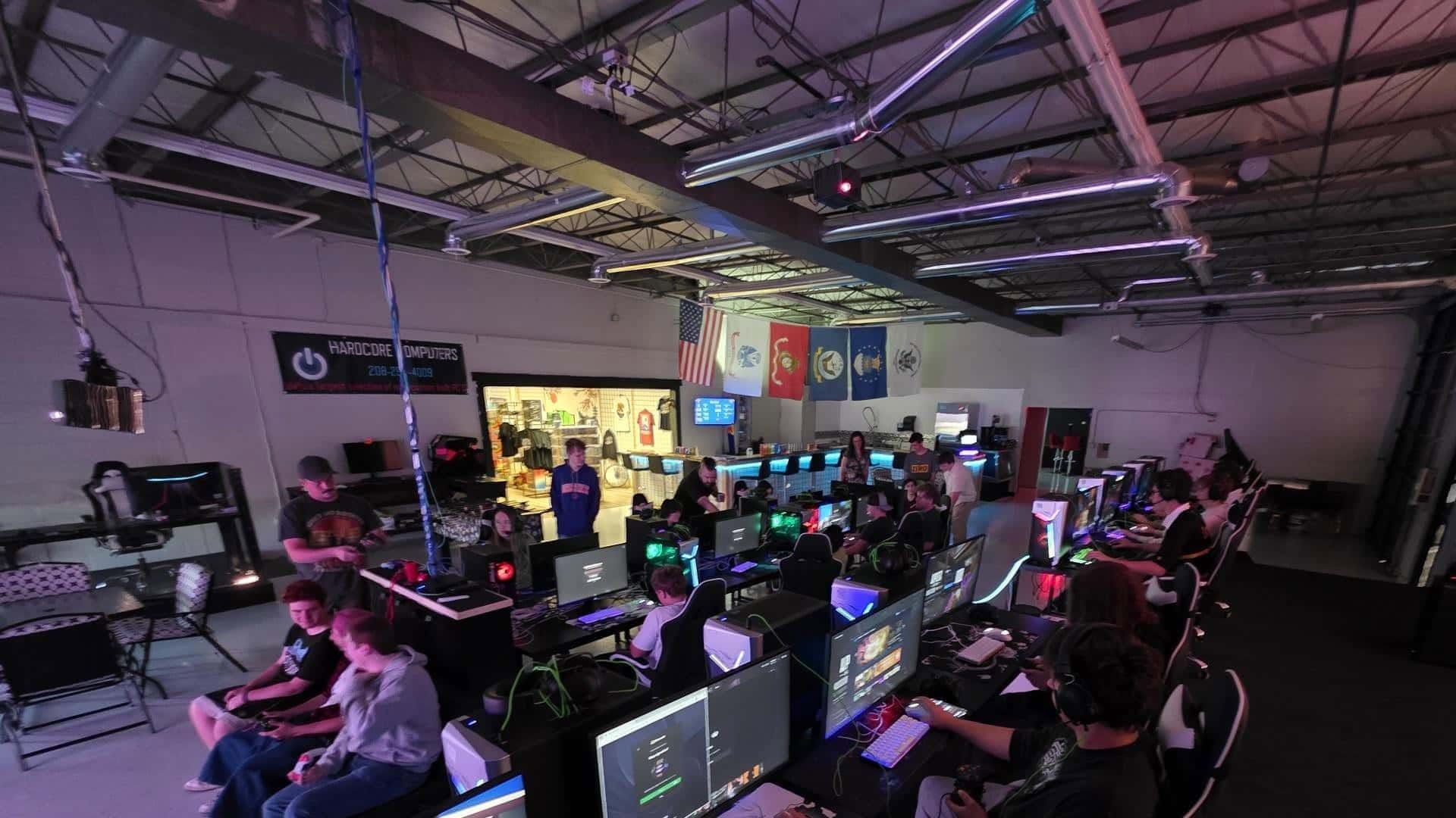 Gaming event room with rows of PC monitors and seated players under purple lighting