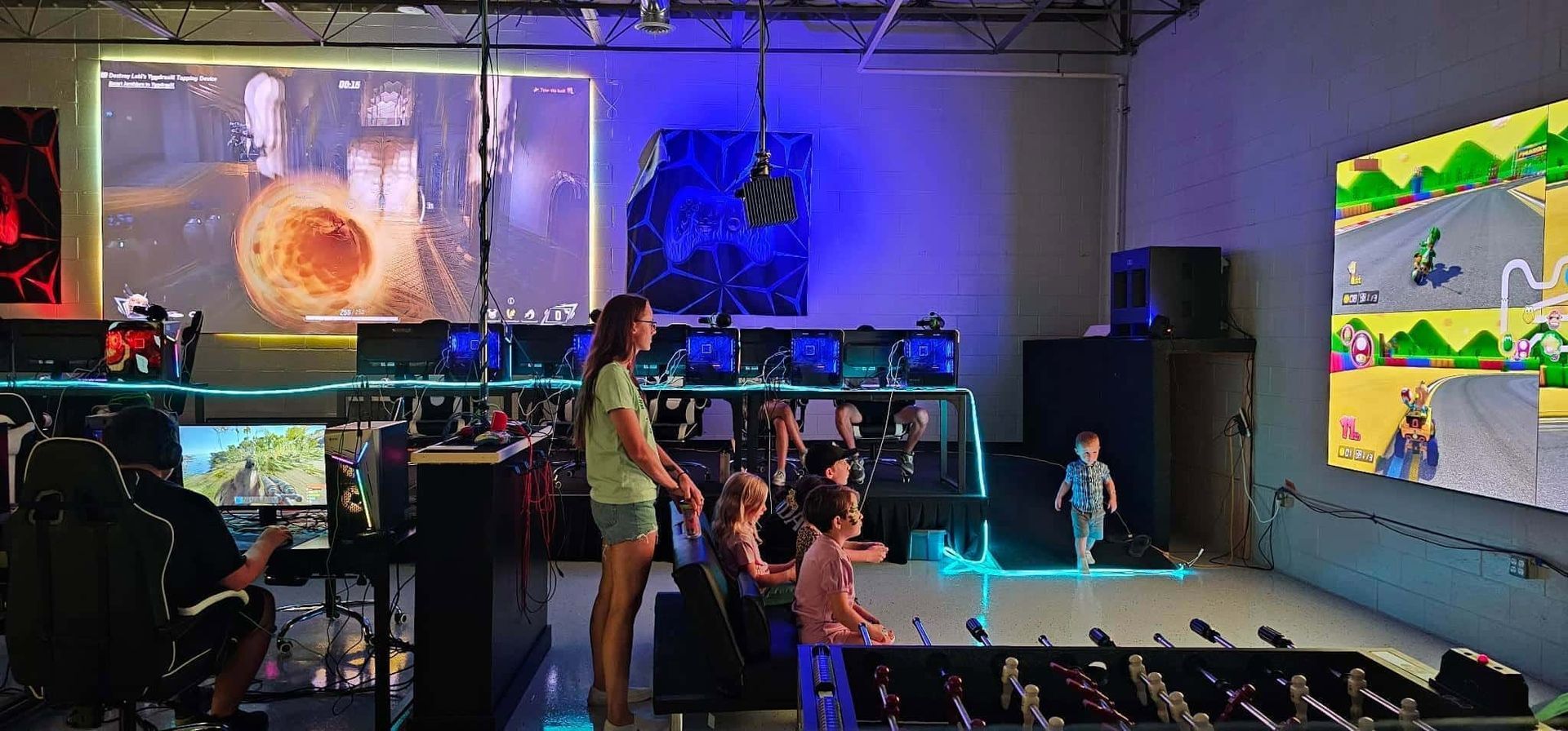 People in a colorful arcade watching a large game screen in a dark room