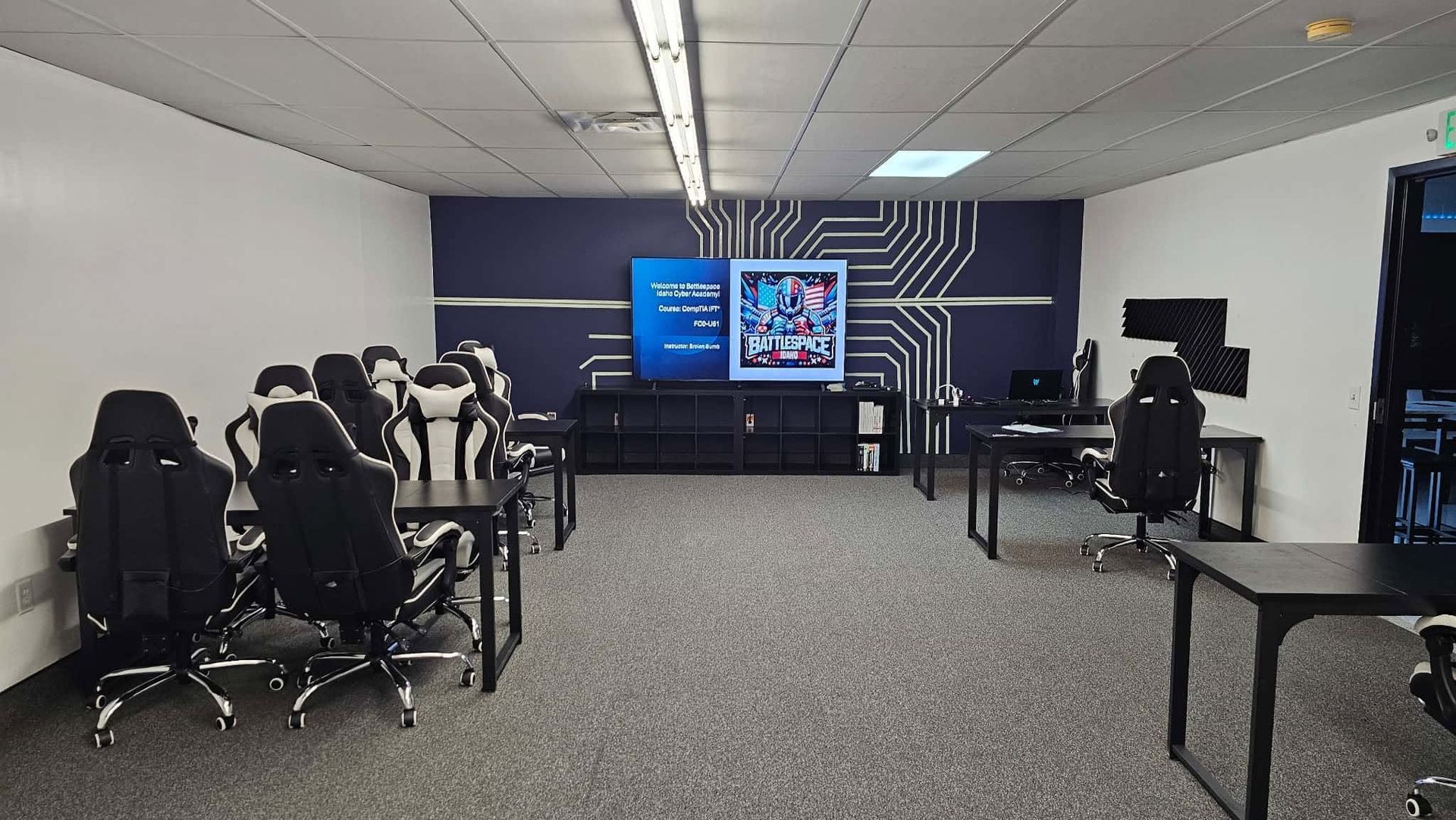 Modern classroom with rows of desks facing a large screen and whiteboard, computer workstations along the walls