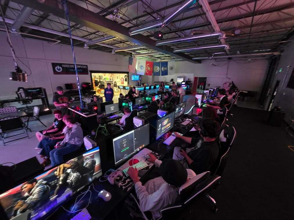Large gaming event with rows of lit computer stations and players in a dim indoor venue