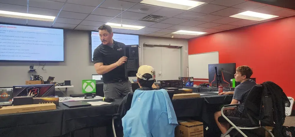 Instructor presenting in a computer lab classroom with students seated at desks and a projected screen.