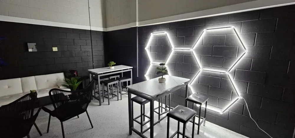 Dim lounge with black walls, glowing hexagon wall lights, and small tables and chairs