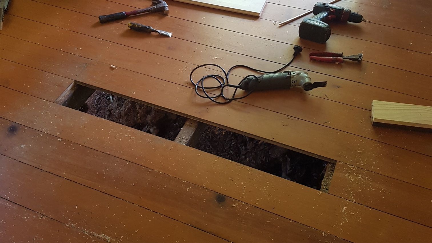 Wooden floor with a rectangular cutout hole and scattered tools, including a saw and cables.
