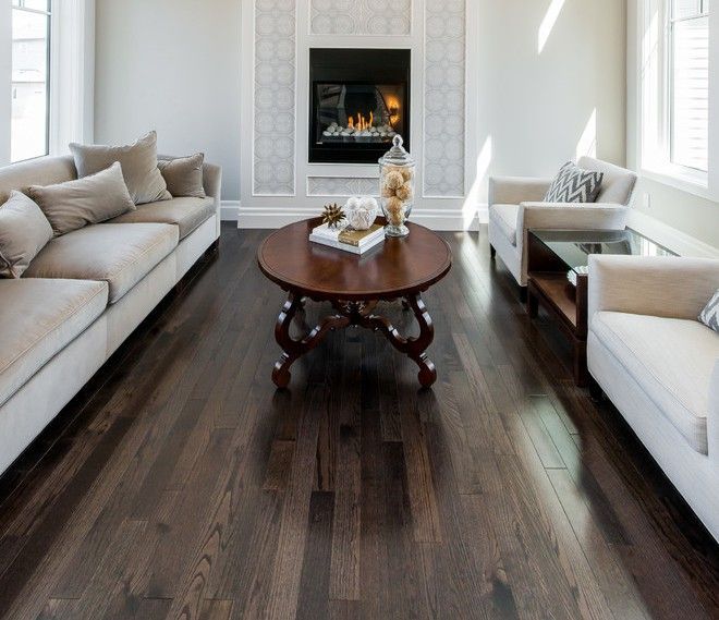 Elegant living room with beige sofas, dark wood floor, round coffee table, and lit fireplace.