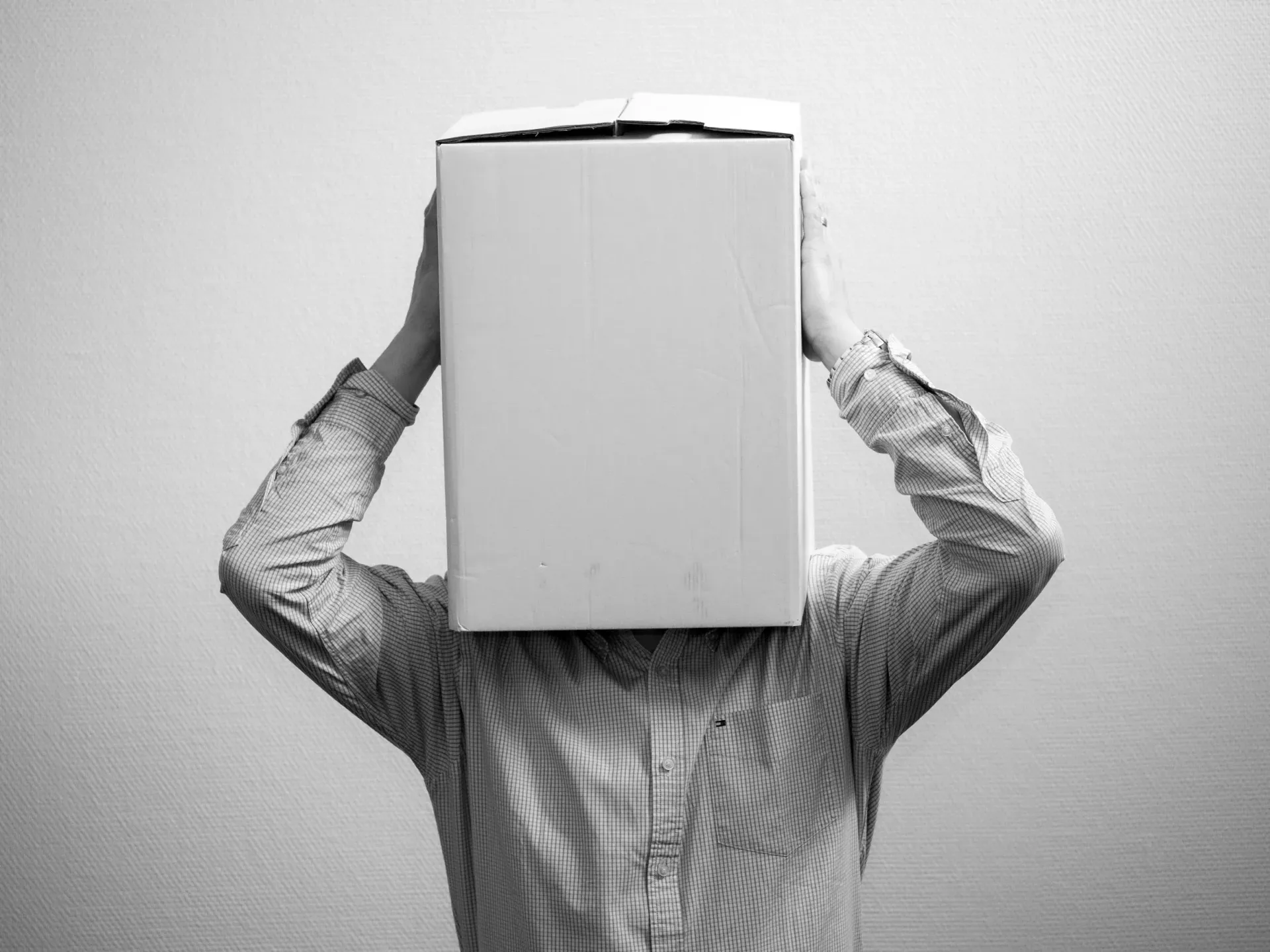 Personne portant une chemise à motifs tenant un grand carré blanc sur son visage, sur fond uni.