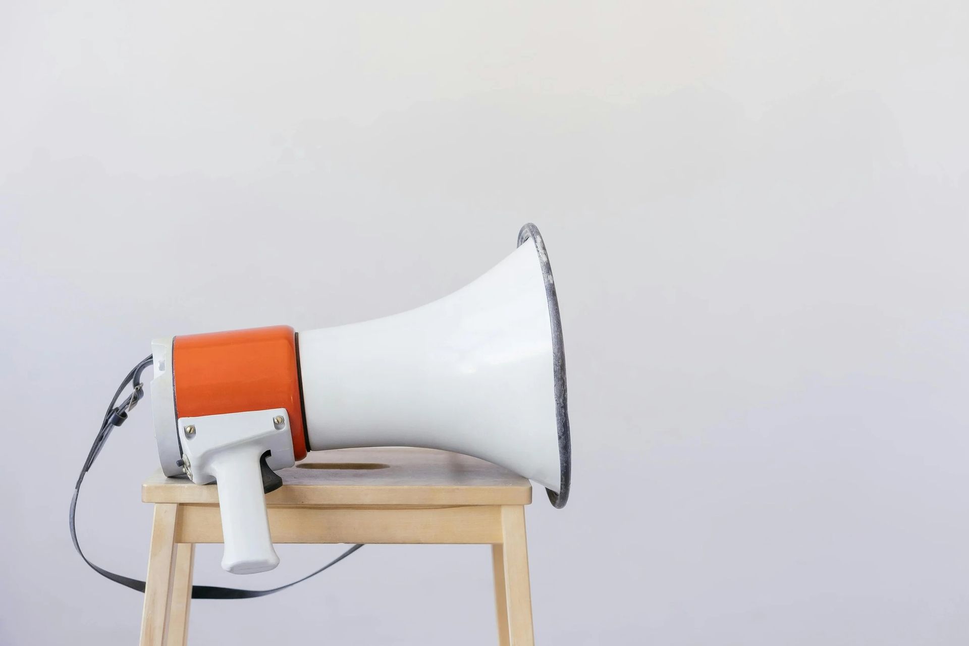 Mégaphone blanc à poignée orange posé sur un tabouret en bois sur un fond clair uni