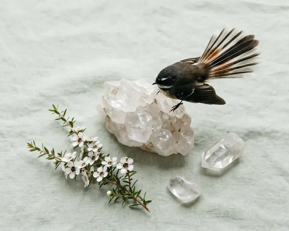 Small bird figurine on white crystal cluster beside tiny flowers and clear stones on a pale background