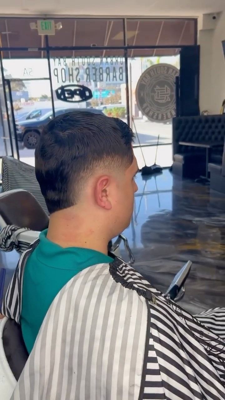 A person in a barber chair wearing a striped cape, displaying a fresh, faded haircut in a barbershop.