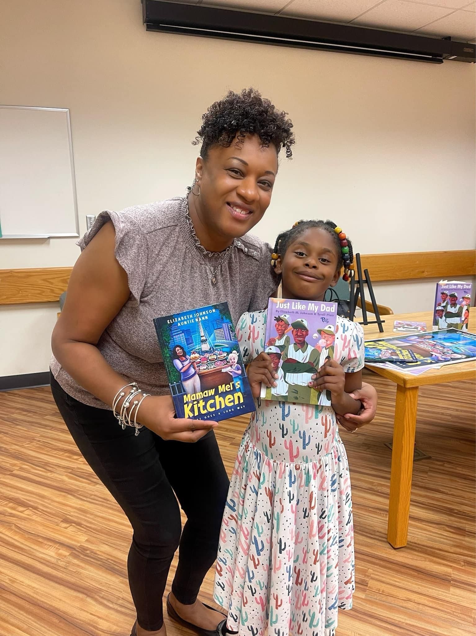 A woman and a little girl are holding books in a room.