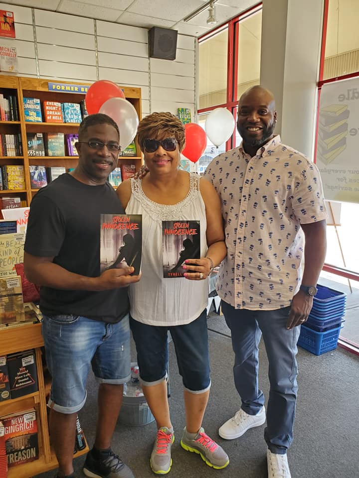Three people are standing next to each other in a bookstore holding books.