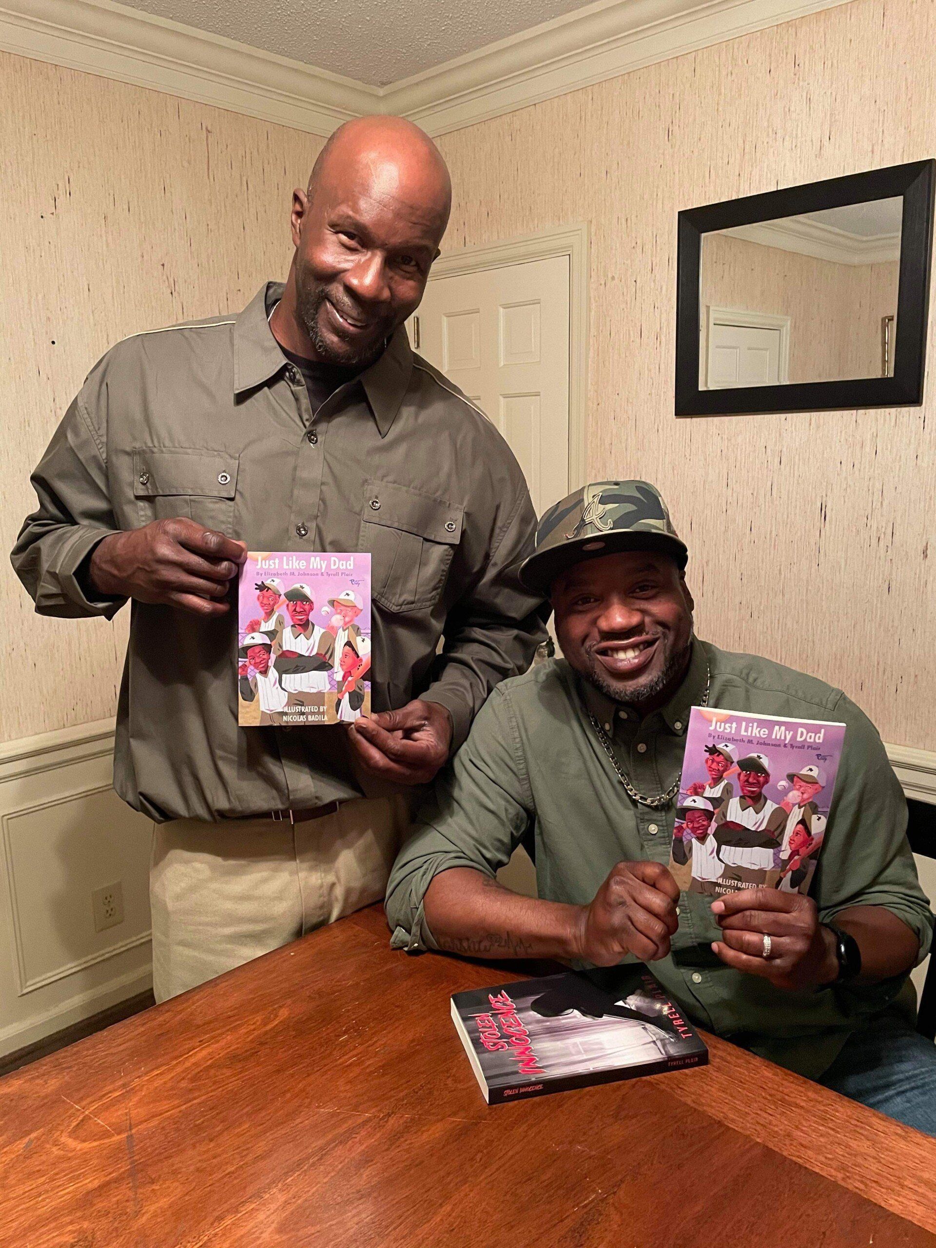 Two men are sitting at a table holding books.