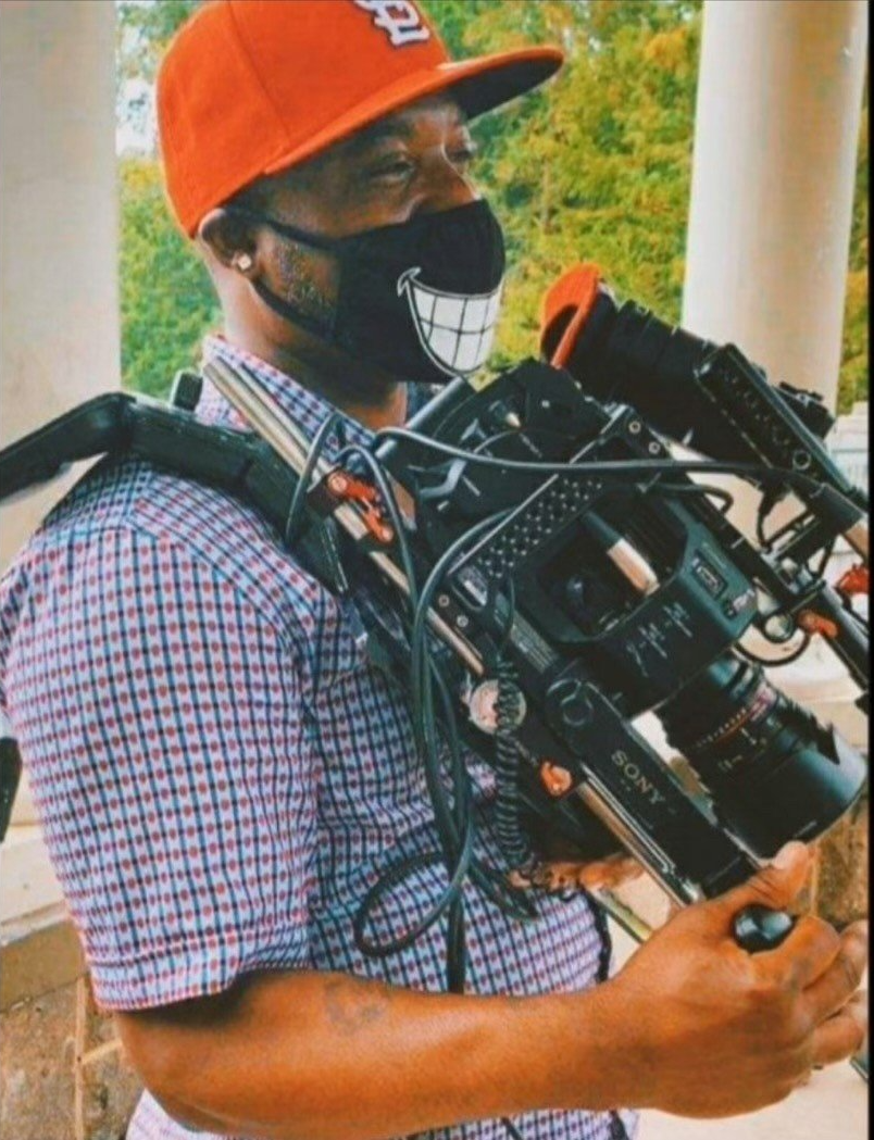 A man wearing a red hat and a mask is holding a camera.