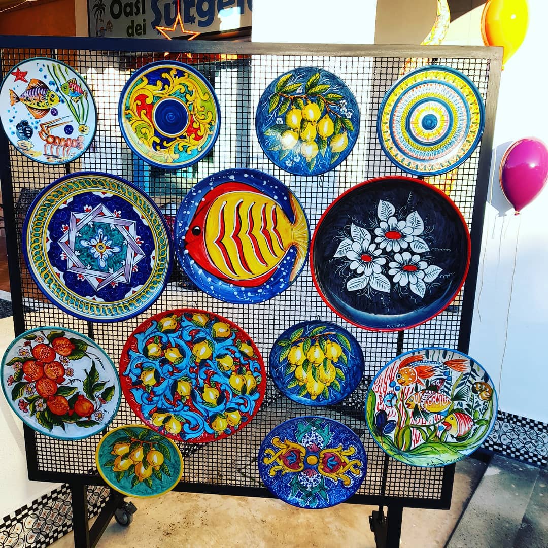 Esposizione di piatti decorativi colorati, dipinti a mano, con motivi di frutta, pesci e fiori.