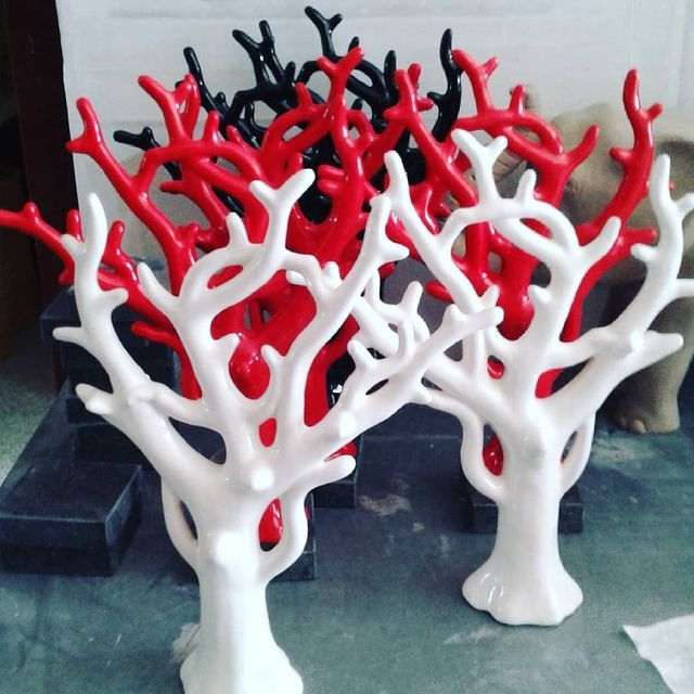 Tre sculture in ceramica a forma di corallo nei colori rosso, bianco e nero su una superficie scura.