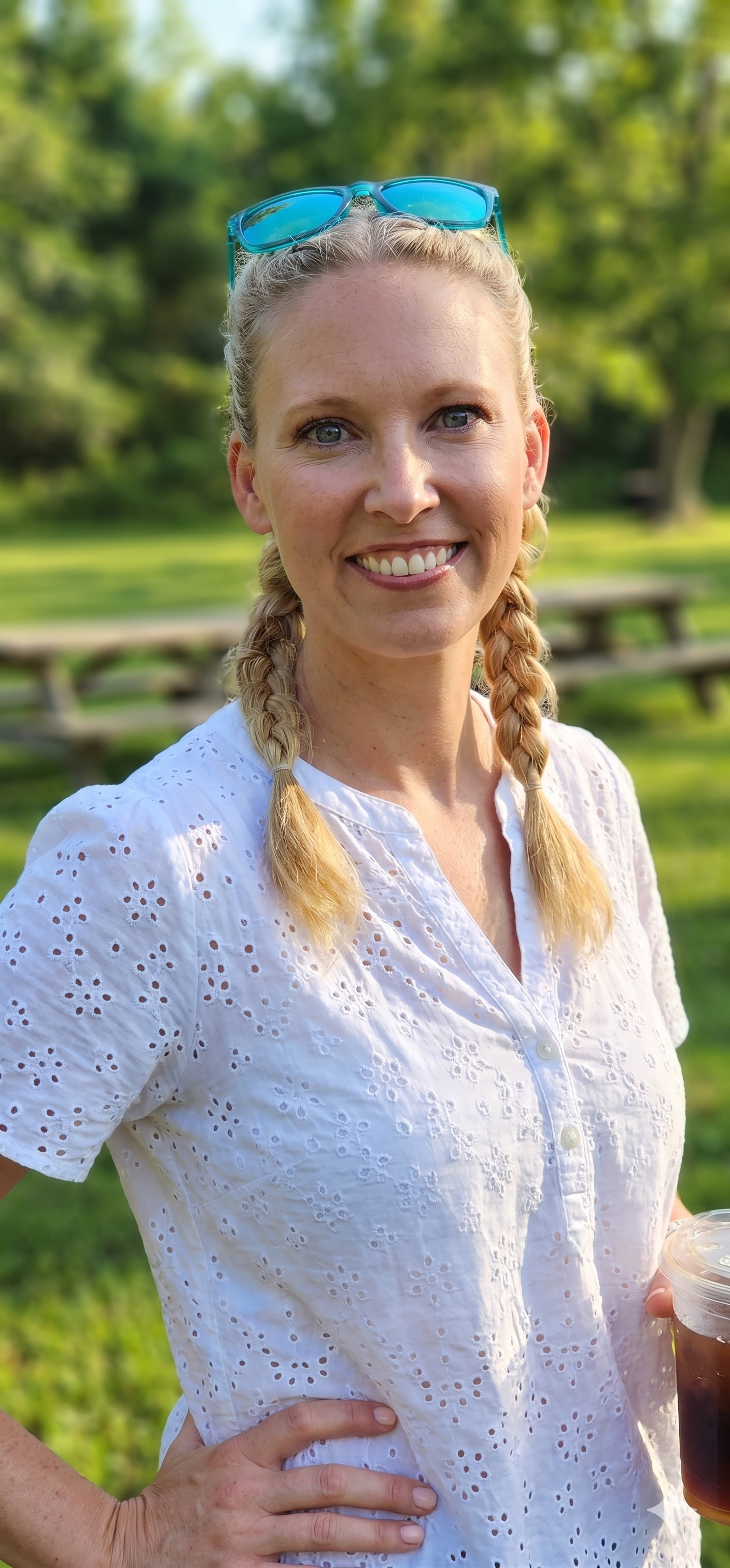 Woman smiling outdoors in a white blouse with braided hair and sunglasses on her head