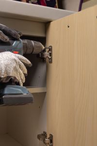 A person is using a drill to fix a cabinet door.