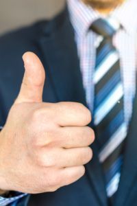 A man in a suit and tie is giving a thumbs up.
