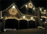 Maison décorée de lumières de Noël blanches et de couronnes la nuit.