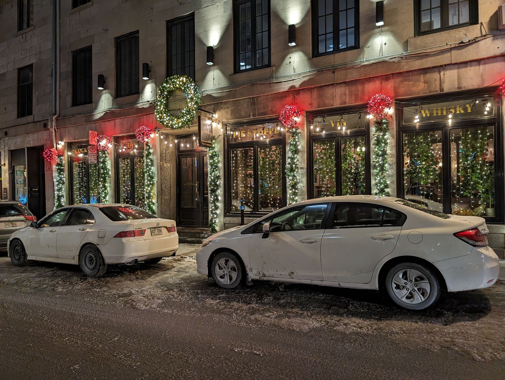 Two white cars are parked in front of a building decorated for christmas.