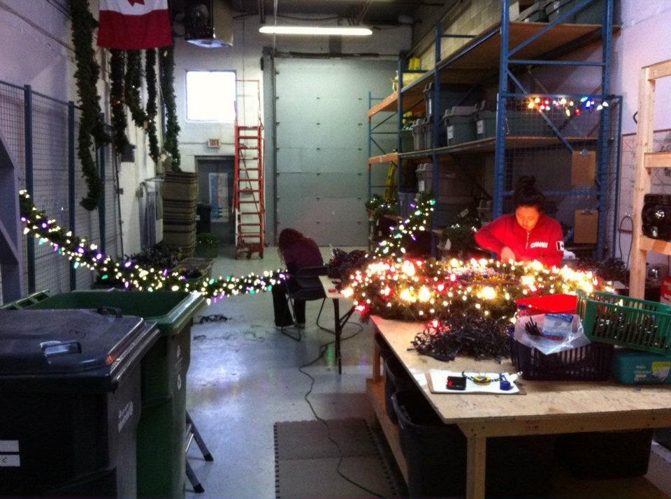 An indoor work area with a person in a red jacket working on Christmas lights.