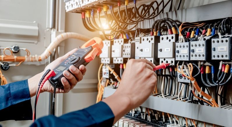 Electrician using multimeter on electrical panel.