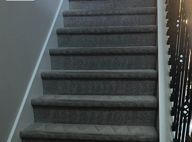 Carpeted indoor staircase with dark railing and gray walls