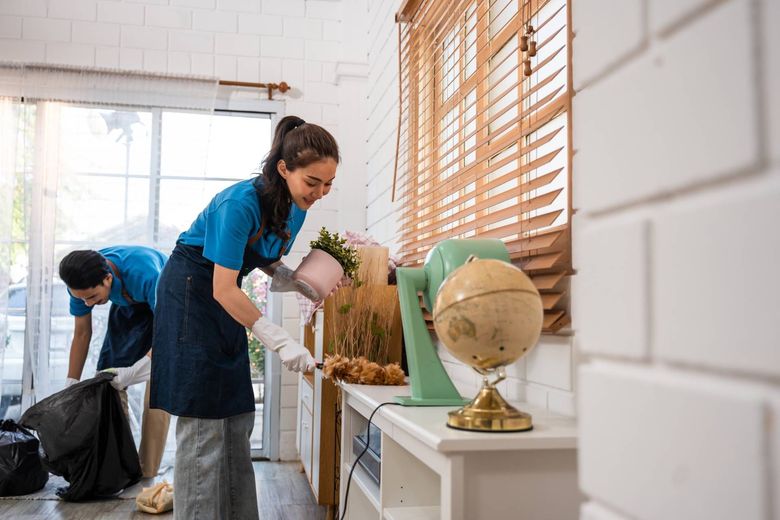 Two people cleaning a bright room with white walls and a globe on a table.