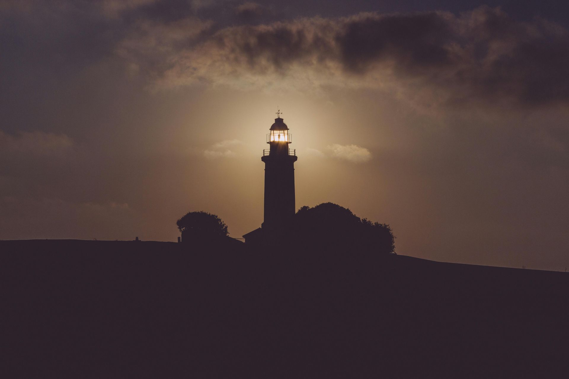 Sunlight bursts through dark, stormy clouds, casting bright rays down.