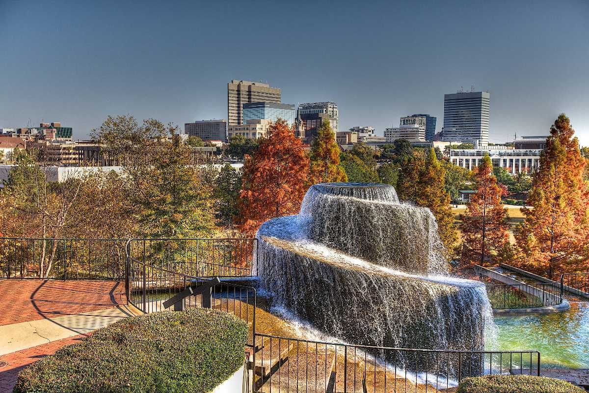 A tiered fountain cascades into a pond; skyline in the background with trees displaying autumn colors.