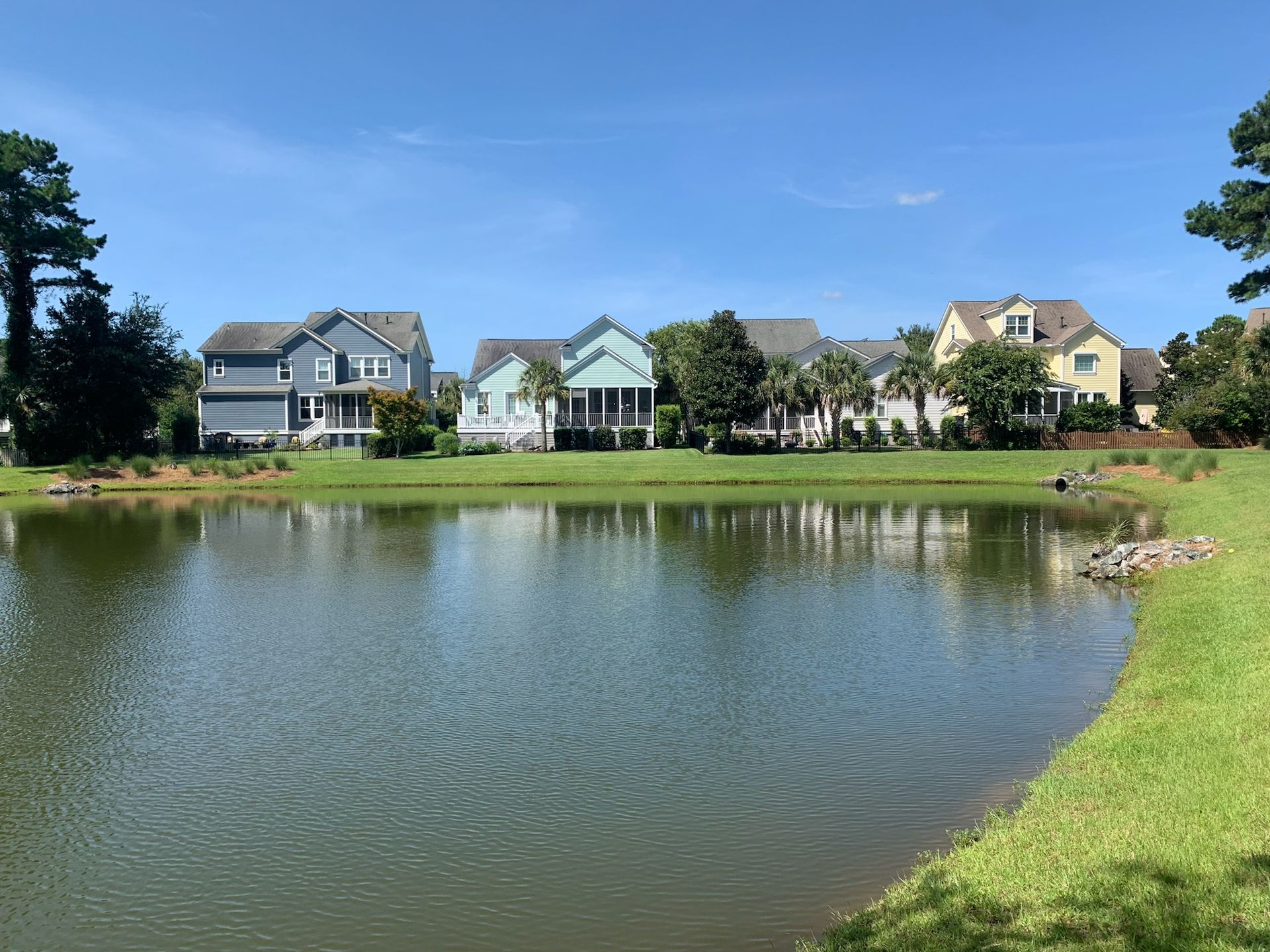 Houses line a pond with green grass on a sunny day.