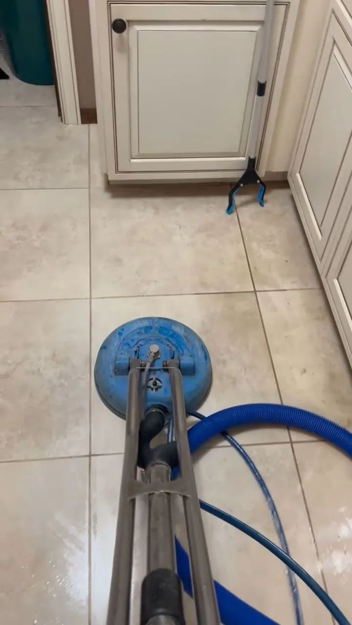 Blue floor-cleaning machine on tiled kitchen floor near cabinets and hoses