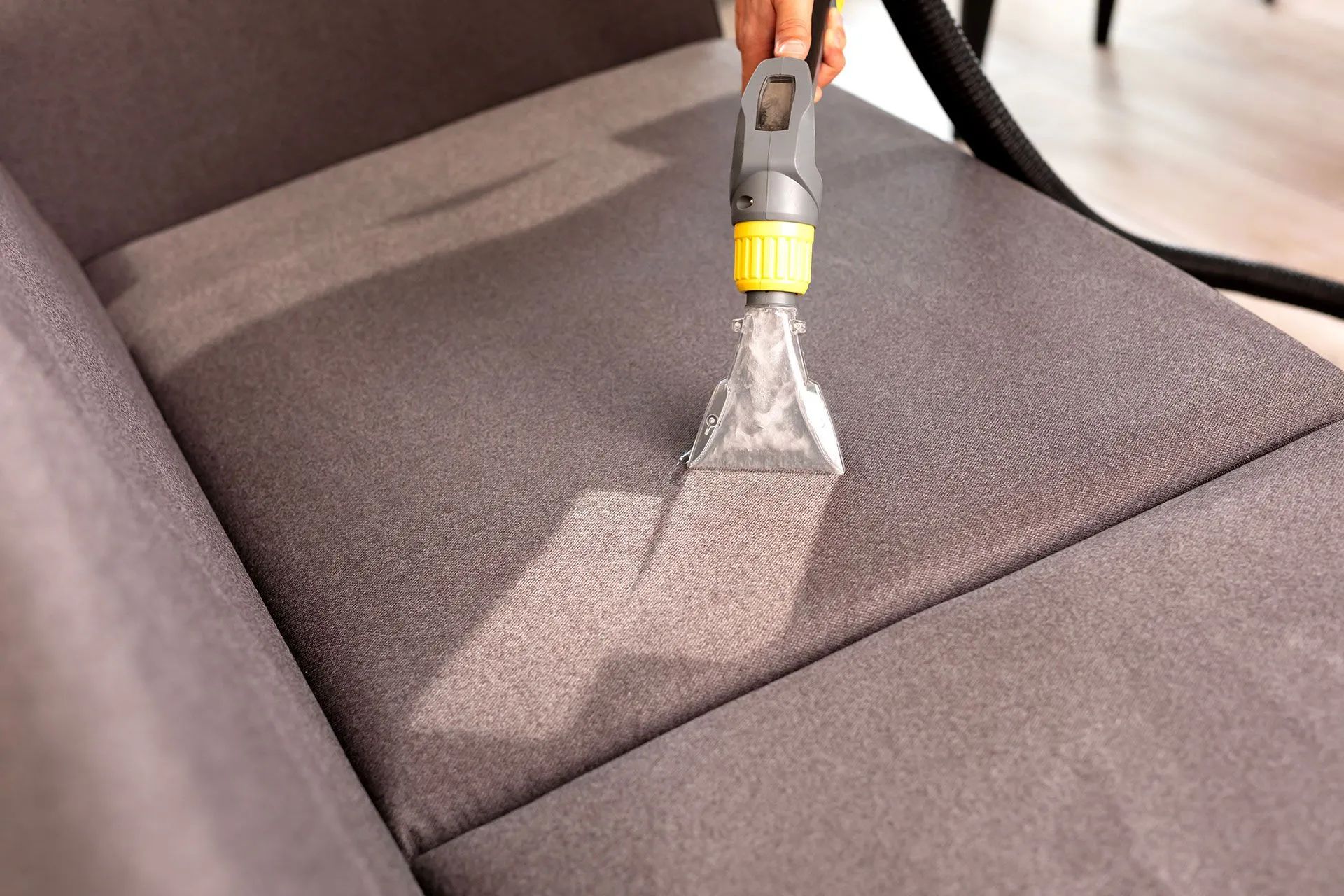 Car seat being cleaned with an upholstery extractor, showing a wet cleaned patch on gray fabric.